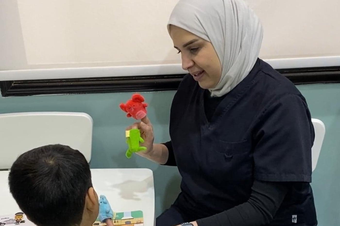 أخصائية تستخدم دمى الأصابع مع طفل في جلسة فردية على طاولة صغيرة في مركز الفارس الصغير